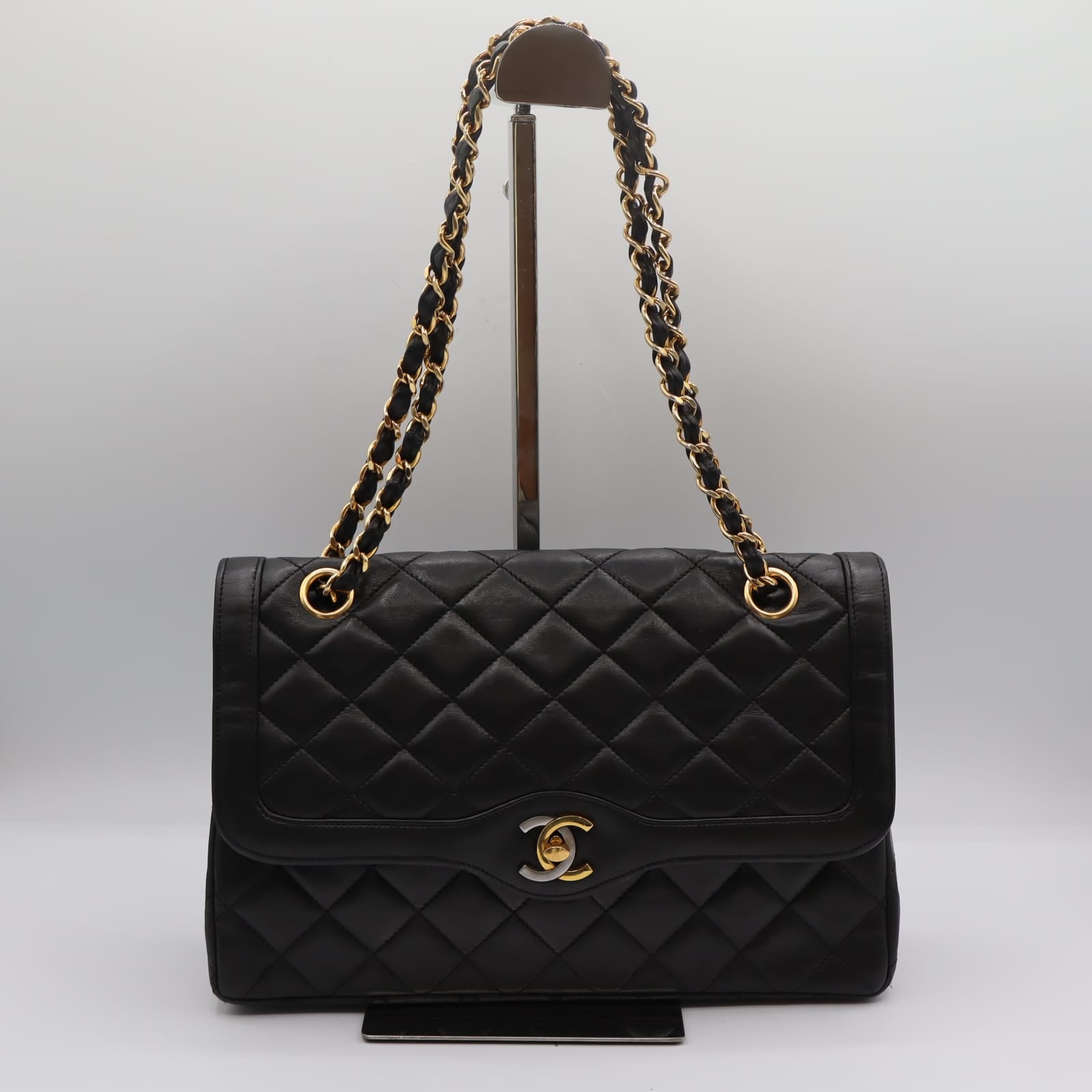 Sac Chanel Double Rabat en cuir noir matelassé, chaîne dorée entrelacée de cuir, posé de face sur fond neutre.