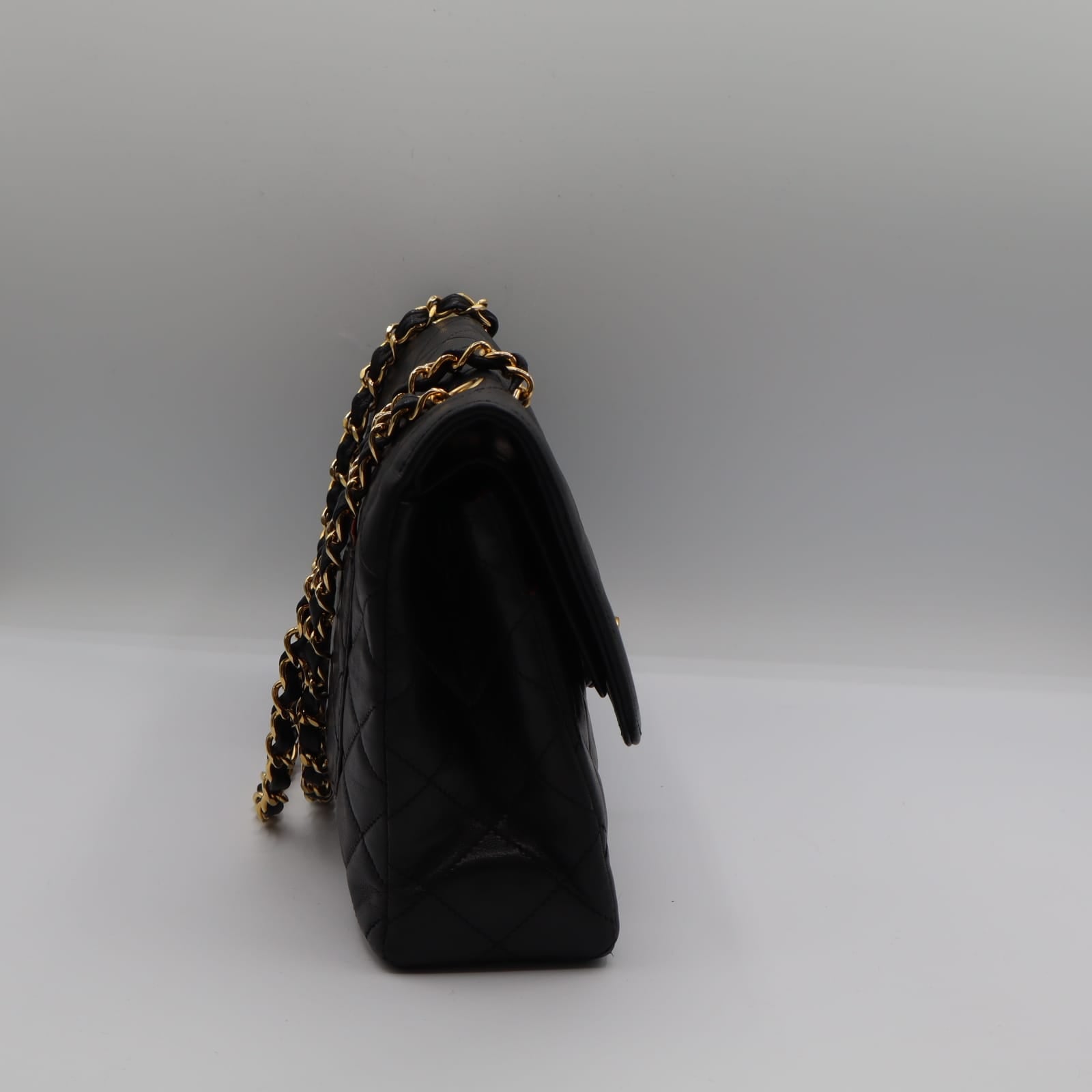 Sac Chanel Double Rabat en cuir noir matelassé, chaîne dorée entrelacée de cuir, posé de profil sur fond neutre.