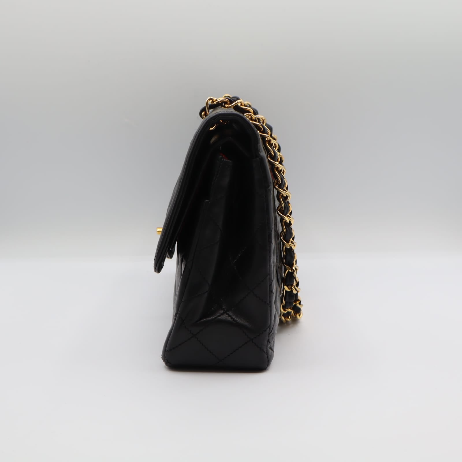 Sac Chanel Double Rabat en cuir noir matelassé, chaîne dorée entrelacée de cuir, posé de profil sur fond neutre.